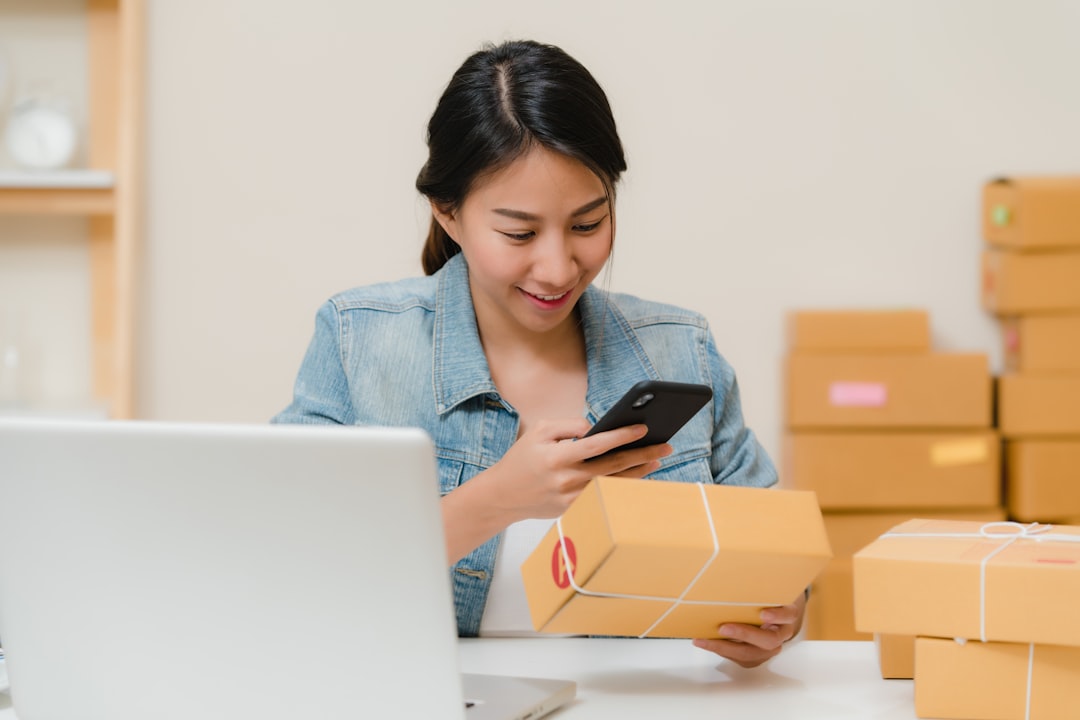 e-commerce packaging - Woman checking package with phone near laptop and boxes