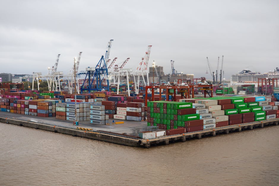 A bustling shipping port with stacked cargo containers and cranes under overcast skies.