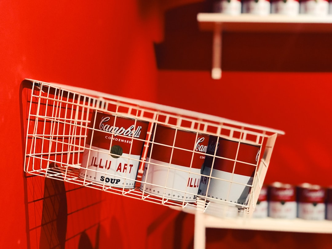 private label packaging - a red wall with a white wire basket holding cans of coca - cola