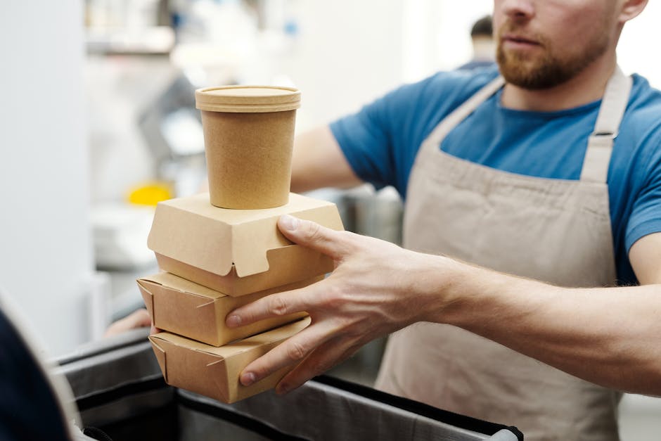 mono-material packaging - Man wearing apron stacks eco-friendly food containers for takeaway delivery in a kitchen setting.