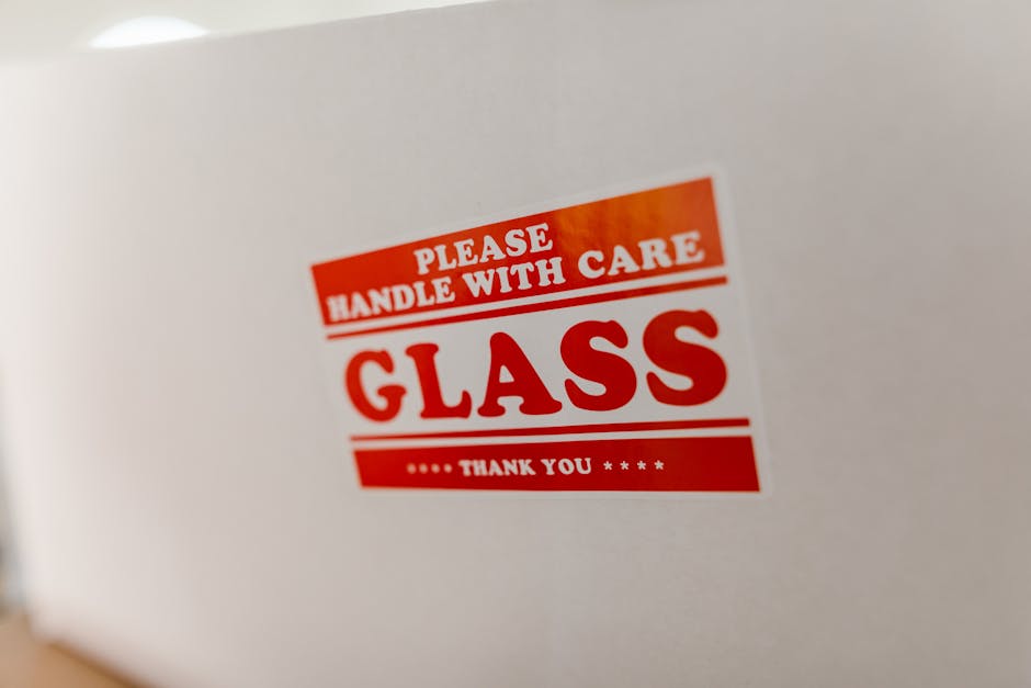 packaging typography - Close-up of a glass packaging label with 'Handle with Care' warning text on a white box.