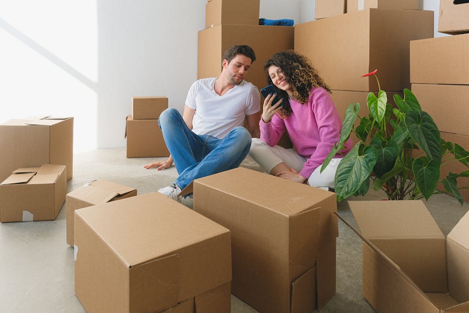 smart packaging technology - Young couple sitting among cardboard boxes, looking at smartphone, symbolizing moving or relocation.