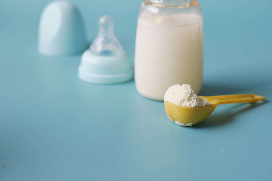 baby product packaging - Close-up of baby milk formula powder in a yellow scoop with a bottle on a blue background.